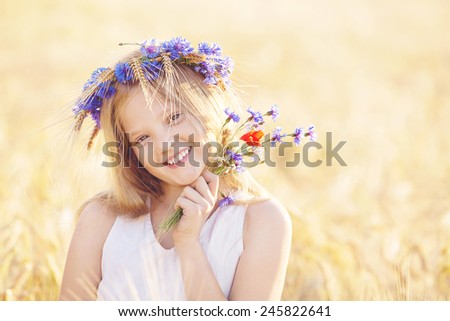 Portrait of beautiful happy blond, Caucasian girl with blue eyes smiling. Teenager with flowers crown in golden wheat field.