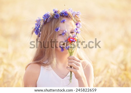 Portrait of beautiful girl with flowers crown smelling fields flowers outdoors. Concept of pollen allergy.