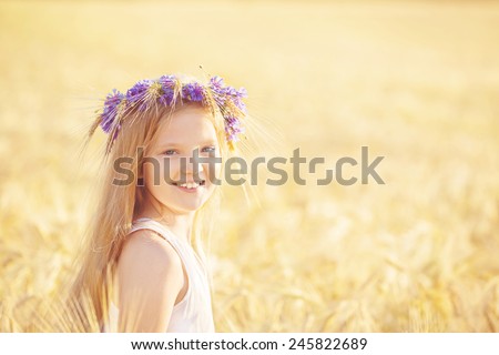 Happy girl with flowers crown at wheat summer field, at sunny day
