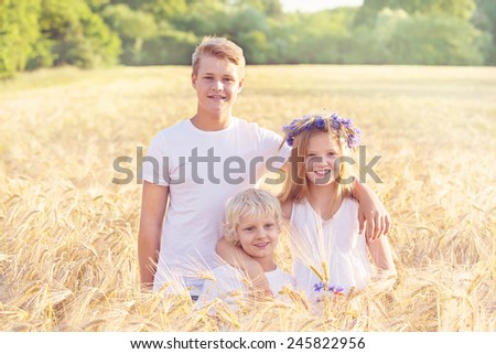 Family of three children, siblings hugging in the wheat summer field. Happy children hugging, concept of relationship and togetherness.