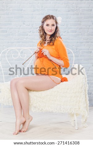 Pregnant woman knitting, with open legs. Maternity studio shot