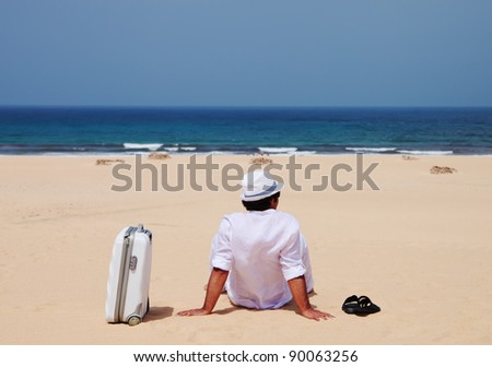 Man siting with luggage on a sand and observing sea