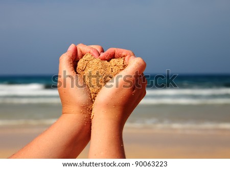 Hands holding a sand with a heart towards sea