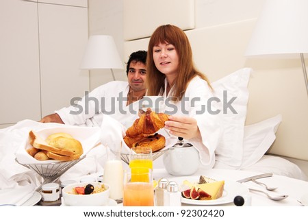 Young happy couple having breakfast in bed, eating croissants