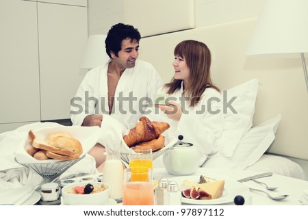 Young happy couple having breakfast in bed, eating croissants
