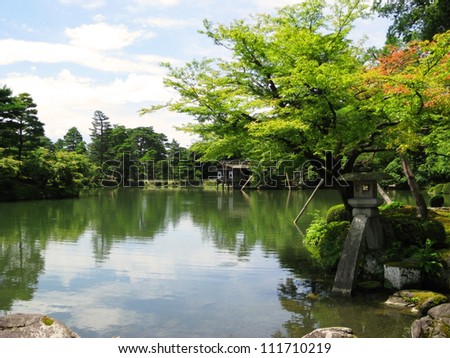 A big pond with an old building behind a beautiful colorful tree in the Kenrokuen Garden - Japan One of the three most beautiful gardens in Japan