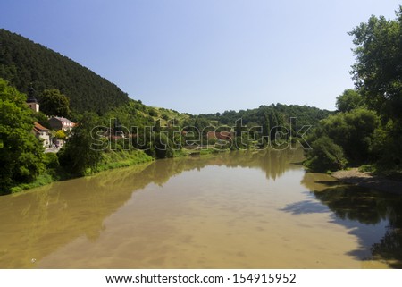 A river in the czech countryside surrounded by trees and meadows with a couple of small family houses.