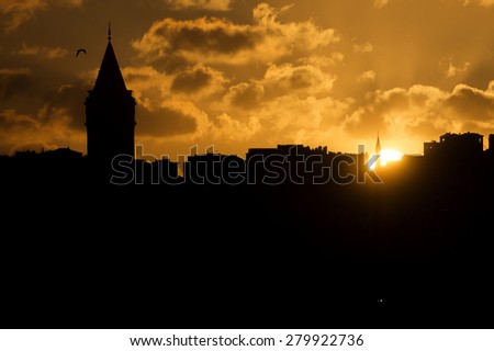 Black silhouette of a Galata tower and nearby buildings against a golden sunset