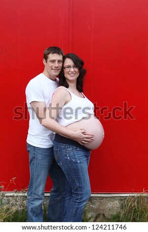 Maternity photos of a couple with red doors as a background - 8 months pregnant