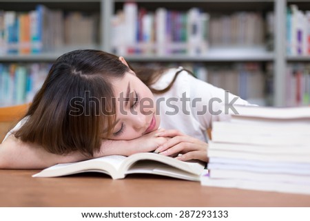 Beautiful asian female student take nap in library during studying stack of books.
