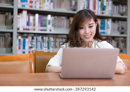 Beautiful asian female student using laptop for study in library with bookshelf background.