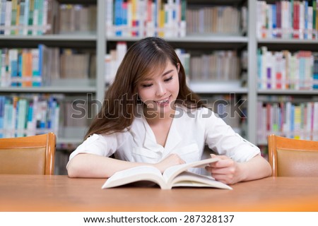 Beautiful asian female student read book in library with bookshelf as background.