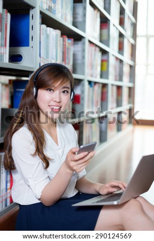 Asian beautiful female student listen music and using laptop in library