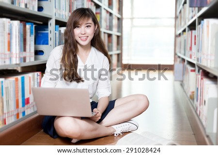 Asian beautiful female student studying in library with laptop