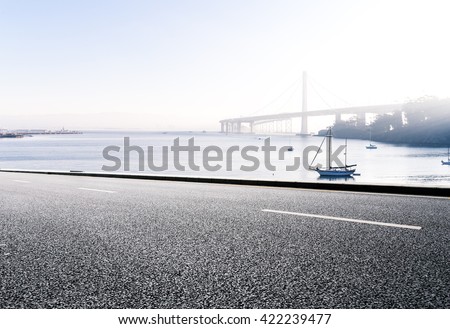 empty asphalt road with sail boat on tranquil water and distant gold gate bridge