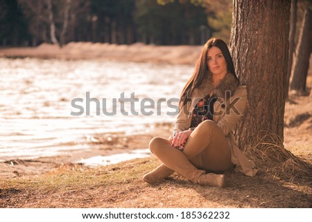Brunette girl sitting cross-legged under the tree on a lake shore lit by evening sunlight