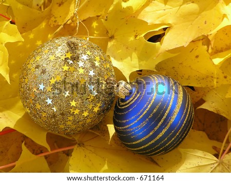 Blue and golden Christmas balls with golden swirls and starts in maple leaves on a sunny day