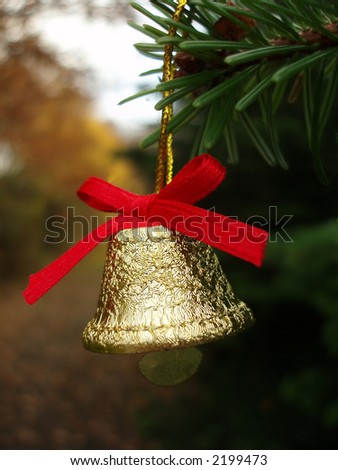 Golden Christmas bell with red band on Christmas tree in forest