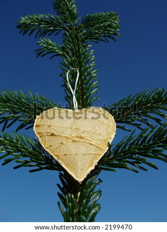 Christmas heart with golden decorations on green spruce tree against clear blue sky