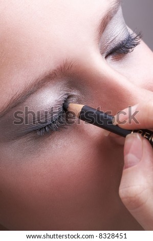 makeup artist tracing black contour of a girl\'s eye, blue eye powder
