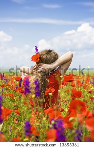 girl with flowers in her hair in the middle of a field with poppies and violet flowers, looking at the horizon