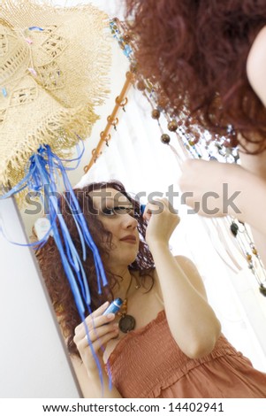 woman putting on mascara, looking in the mirror