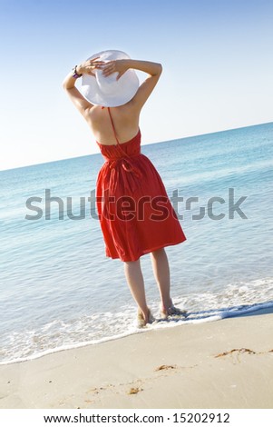 woman in red dress and white hat standing on the beach and looking at the horizon