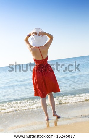 woman in red dress  and white hat looking at the horizon over blue sea