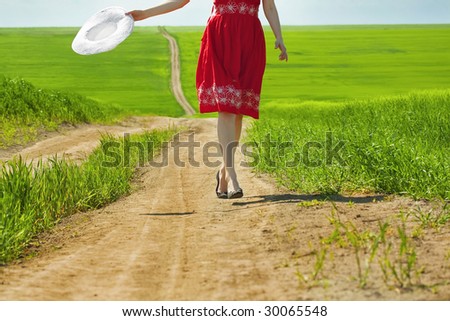 woman in red dress holding white hat walking on an empty country road