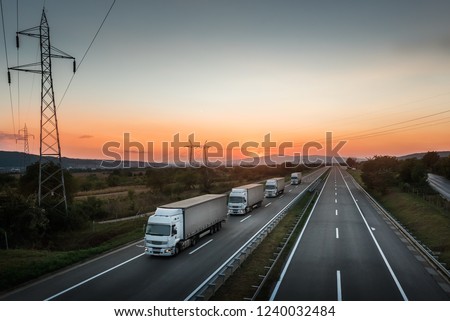 Four White Lorry Trucks Convoy on highway at beautiful sunset