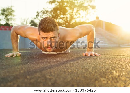 Handsome guy doing push-ups outdoors on a sunny summer day