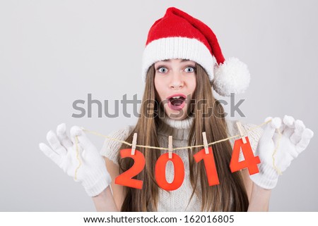 Happy surprised beautiful young Caucasian Santa girl holding New Year number decoration. Christmas and New Year celebration concept. Surprised facial expression.