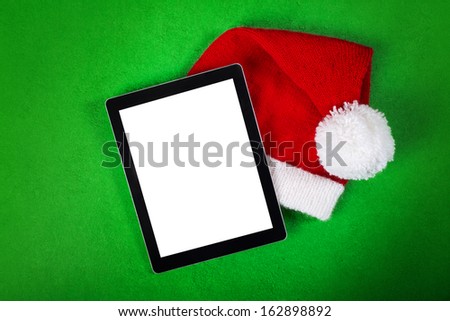 Blank tablet and Christmas Santa hat placed on grungy textured green background. Copy space available in the background and on tablet screen.