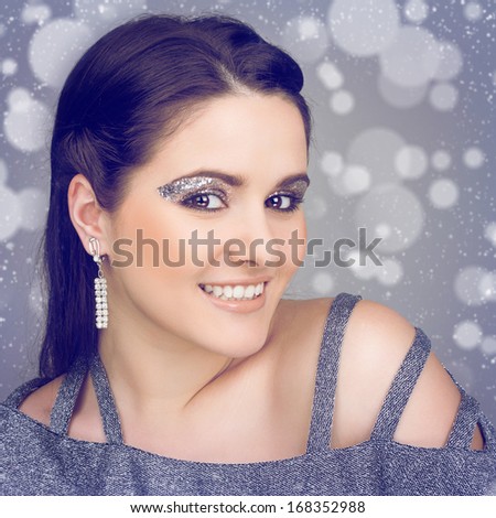 Glamorous happy young Caucasian brunette woman smiling looking at camera wearing glitter makeup and sparkling earring against blurry background. Beauty, makeup and elegance concept.