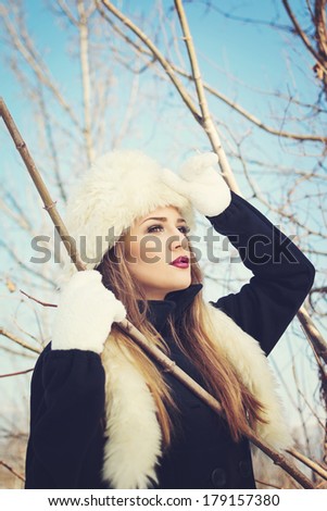 Closeup beauty portrait of a young woman with white fur hat and gloves. Beautiful woman outdoors in winter posing looking up wearing burgundy color lipstick.