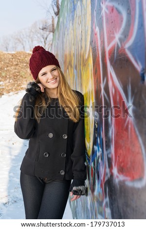 Happy beautiful young Caucasian blonde teenage girl outdoors winter portrait. Model posing outdoors in winter against graffiti wall. Teenage lifestyle concept.