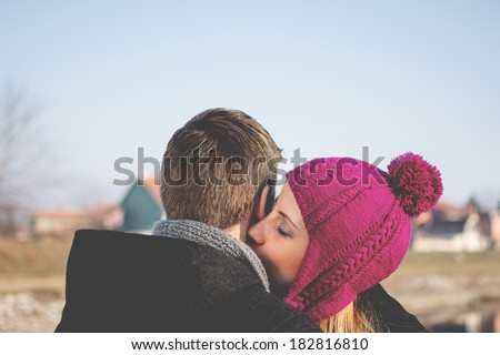 Closeup outdoors portrait of young woman kissing her boyfriend\'s neck. Happy people in love kissing and enjoying outdoors in winter. Copy space available. Love, romance, togetherness concept.