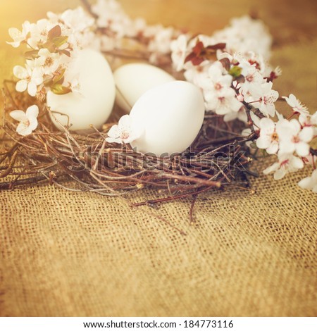 Nest with white Easter eggs and beautiful Spring flowers decoration. Nest placed on jute decoration on the table. Closeup shot with back light. Easter holiday and Spring concept.