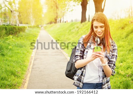 Happy beautiful young Caucasian redhead high school girl with green smart phone outdoors on sunny summer day texting and smiling.