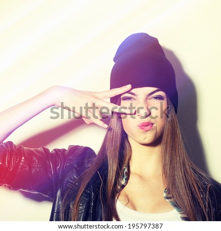 Closeup studio shot of pretty hipster teenage girl with beanie hat pouting gesturing peace. Square image with instant filter applied.