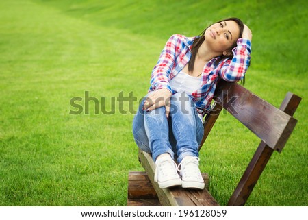 Cute young Asian brunette woman in park sitting on the bench in park in summer relaxing wearing casual everyday clothes.