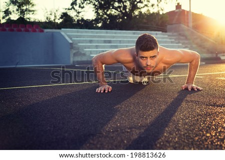 Handsome young shirtless Caucasian fitness man doing push-ups outdoors on sunny summer day. Back lit horizontal image.