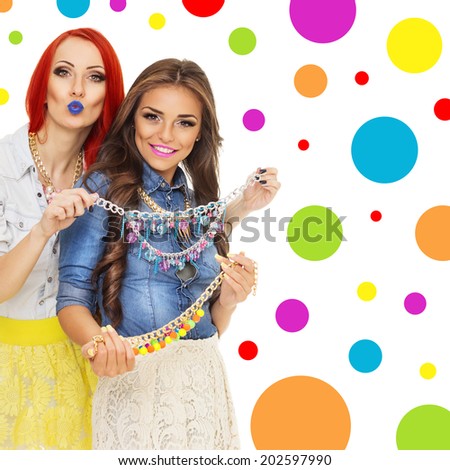 Two happy fashionable young women with colorful modern necklaces wearing denim shirts and lace skirts. Trendy Hispanic and Caucasian brunette girls smiling wearing purple and pink lipstick isolated.