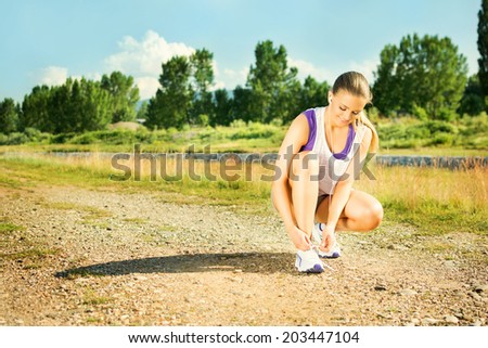 Beautiful fit young runner woman tying shoe laces outdoors in summer during jogging. Attractive girl running outdoors in park. Sunny summer day. Horizontal image.