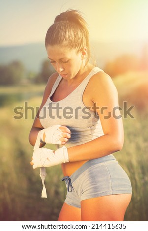 Young woman boxer with hand wraps. Attractive young boxing girl putting bandages on outdoors on sunny summer day.