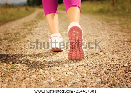 Closeup of woman running shoes on running track outdoors on sunny summer day. Woman in pink shoes and pants jogging in nature. Rear view.