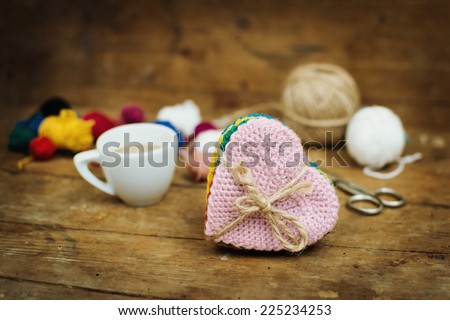 Closeup of vintage crocheted colorful heart shaped coasters, wool yarns and coffee cup on brown wooden surface. Horizontal image.