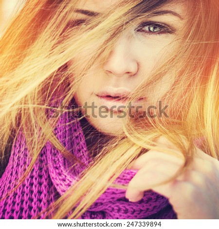 Closeup head shot of beautiful young green eyed blonde woman with purple scarf and flying hair posing. Square format, filter, instagram look, vibrant warm colors.