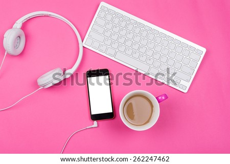High angle view of white wireless keyboard, smart phone with isolated white screen, coffee in pink cup and white headphones on pink background. Horizontal, no retouch, copy space.