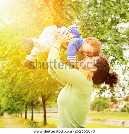 Happy Caucasian mother and son outdoors in park on sunny spring day. Young brunette mother lifting her son in park having fun enjoying motherhood. Square, retouched.